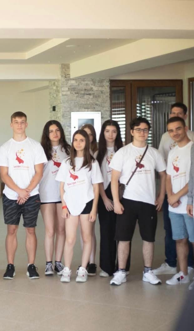 Групна фотографија на ученици во бели маици на Бистри Умови во просторијата на кампот.